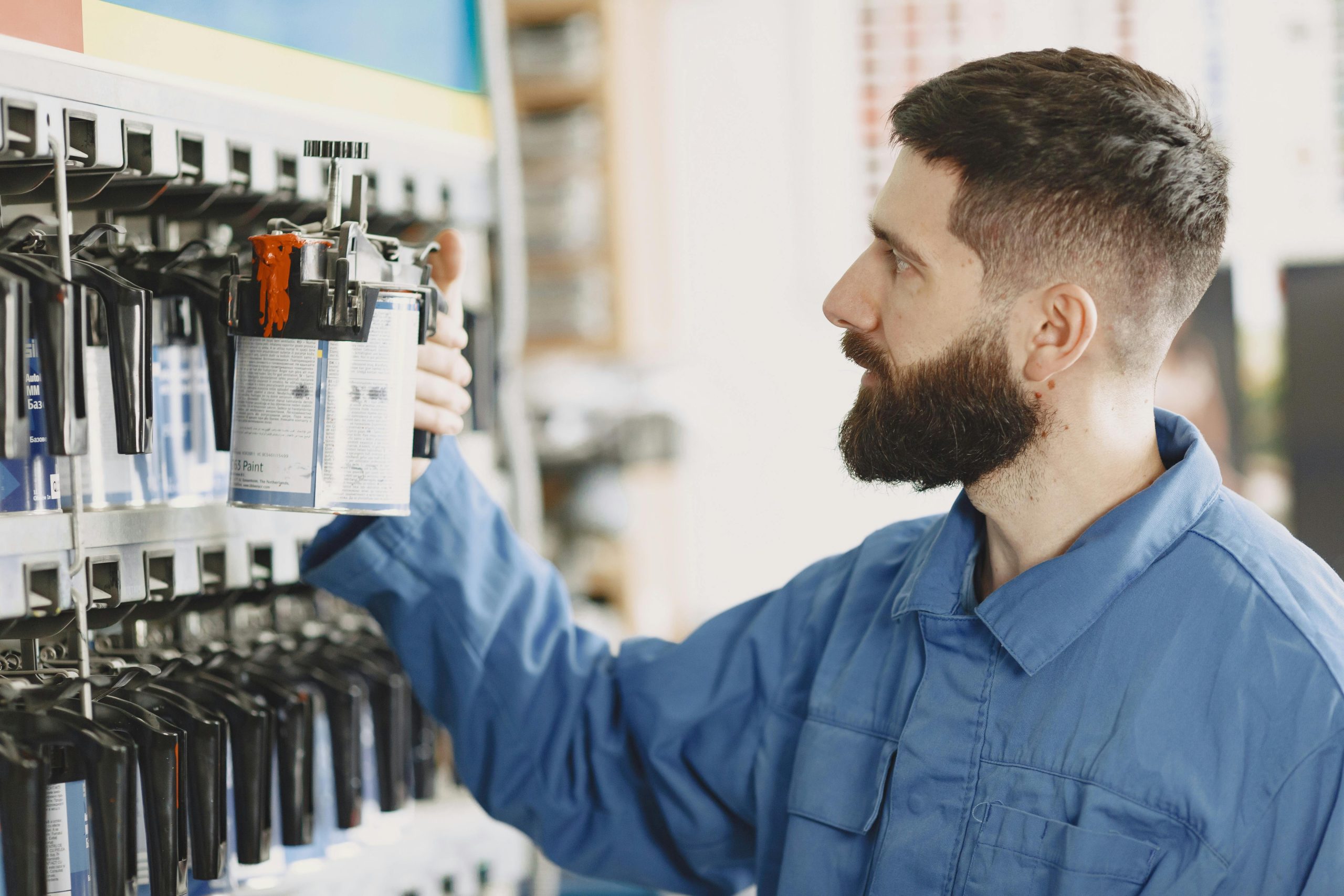 Mechanic in blue overalls choosing a paint can from a shelf in the workshop.