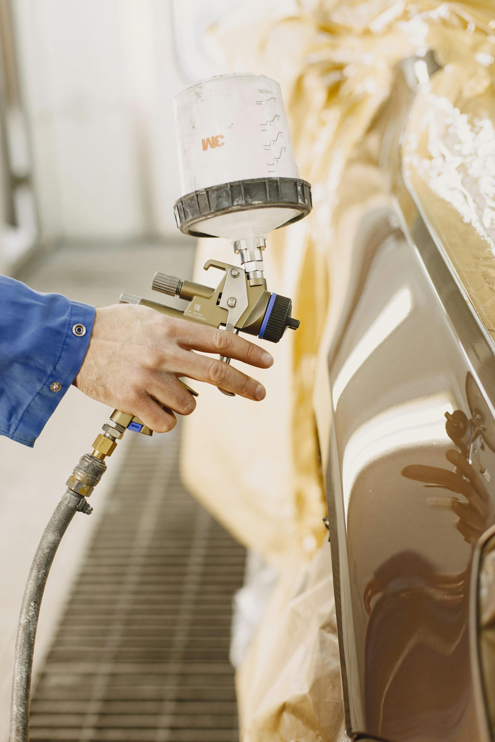 A technician spray paints a car with a paint spray gun in a workshop.